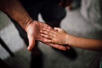 Close-up of a child's hand resting gently on a man's hand, symbolizing love and support. HD wallpaper