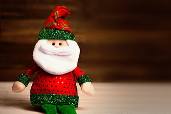 Cute Santa Claus plush toy wearing red and green attire sits on a wooden surface, perfect for holiday decor. HD wallpaper