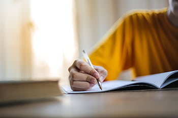 Close-up of a person writing in a notebook, symbolizing focus and learning. HD wallpaper
