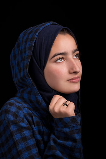 A close-up portrait of a woman wearing a blue plaid hijab, looking thoughtful against a dark background. HD phone wallpaper