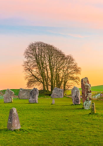 Serene sunset view of Avebury stone circle with vibrant sky and lush green landscape. HD phone wallpaper
