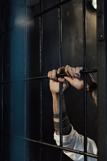 Close-up of hands holding metal prison bars, illustrating confinement and punishment. HD phone wallpaper