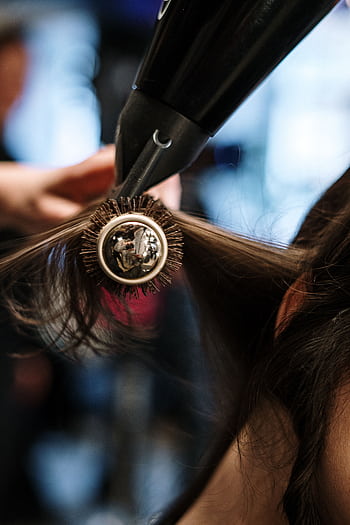 Close-up of a hairstylist styling hair with a brush and dryer in a salon setting. HD phone wallpaper