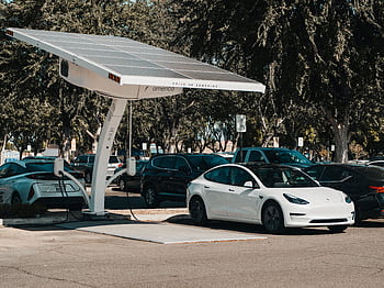 Electric car parked at a solar charging station outdoors, highlighting renewable energy and innovation. HD wallpaper