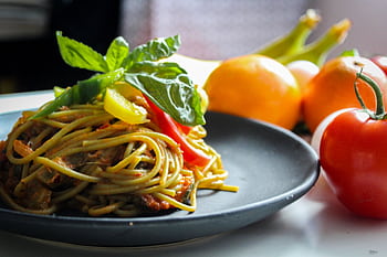 A plate of spaghetti garnished with basil and fresh vegetables, showcasing Italian cuisine. HD wallpaper