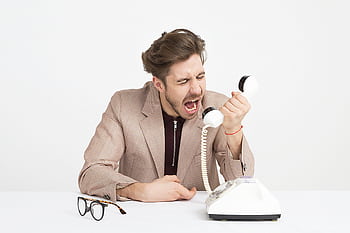 Businessman in a beige suit shouting into a vintage tele, expressing frustration at work. HD wallpaper