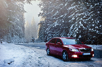 A red car drives along a snowy forest road in winter, surrounded by frosty trees. HD wallpaper