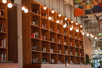 Spacious library with wooden bookshelves and hanging lights in a modern setting. HD wallpaper