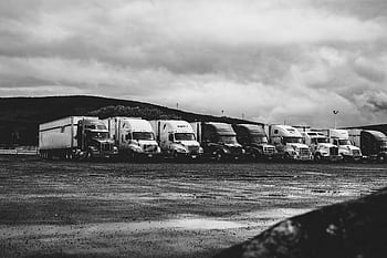 Row of parked semi trucks in a rainy lot, captured in a dramatic black and white setting. HD wallpaper