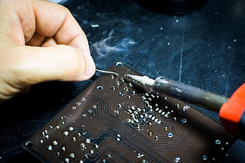 Hand soldering on a printed circuit board, showcasing electronic craftsmanship. HD wallpaper