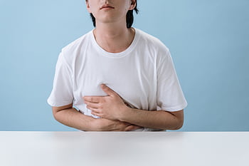 An adult man in a white shirt holds his stomach, indicating pain and discomfort, with a light blue background. HD wallpaper