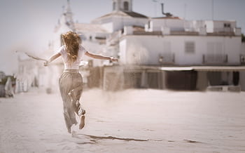 Back view of a young woman jumping and enjoying on a sunny beach, embodying dom and happiness. HD wallpaper