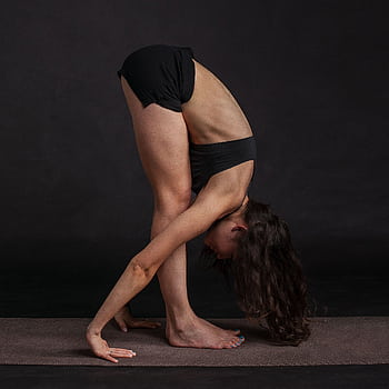 Woman performing forward bend yoga pose on mat, showcasing flexibility and focus. HD phone wallpaper