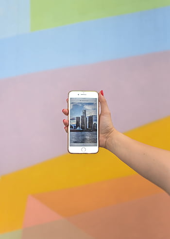 A hand holds a smart displaying a Detroit scene against a colorful wall. HD phone wallpaper