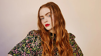 Redhead Sadie Sink Girl Model Is Standing In Light Pink Background Wearing Colorful Flowers Printed Black Dress Girls HD wallpaper