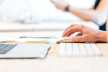 A person working at a laptop with a wireless mouse and keyboard in a bright office setting. HD wallpaper