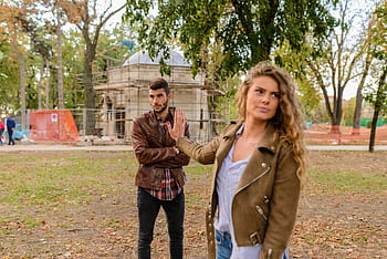 A couple faces disagreement outdoors in a park setting showcasing emotional expressions. HD wallpaper