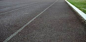 A detailed view of an empty outdoor running track with clear lanes and green grass edge. HD wallpaper