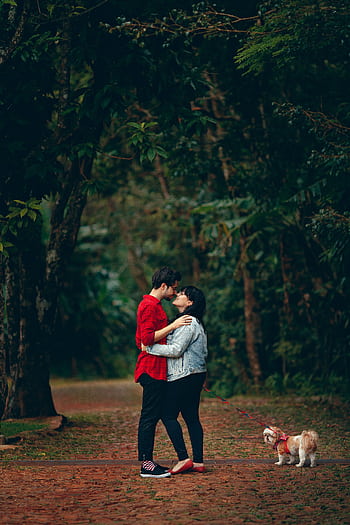 Young couple embracing in a lush forest with their small dog. A moment of affection and togetherness. HD phone wallpaper