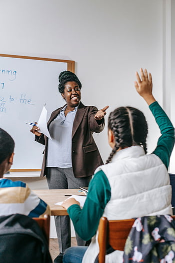 A teacher interacts with students in a classroom, fostering an engaging learning environment. HD phone wallpaper