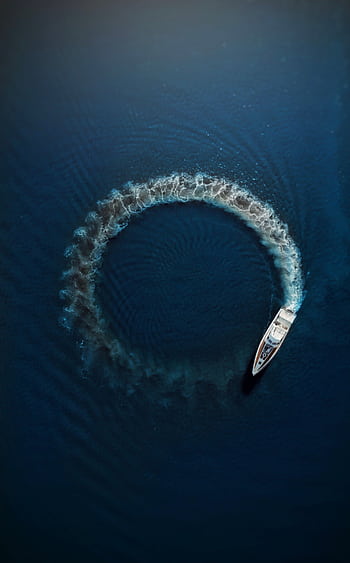 An aerial shot of a motorboat making a circular ripple pattern in the azure ocean water, showcasing motion and summer vibes. HD phone wallpaper