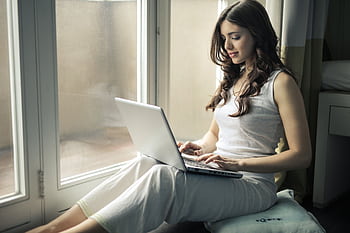 Adult woman sitting by window working remotely on a laptop indoors. HD wallpaper