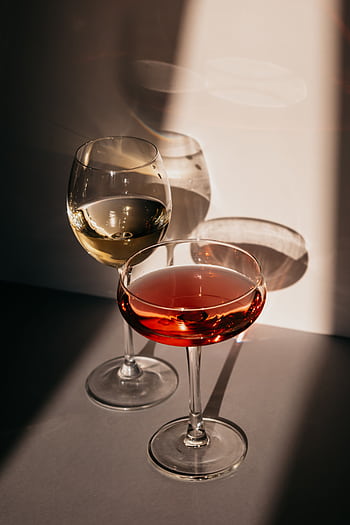 Two elegant crystal glasses with aperitifs casting artistic shadows on a table. HD phone wallpaper