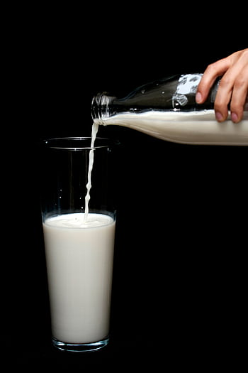 A hand pours fresh milk from a glass bottle into a tall glass with a black backdrop. HD phone wallpaper
