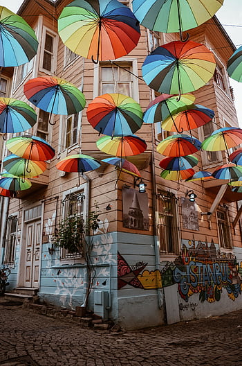 Vibrant umbrellas float above a graffitied street in Istanbul, creating a colorful canopy. HD phone wallpaper