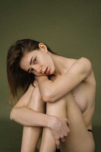 Elegant artistic nude portrait of a woman sitting against a green backdrop, exuding grace and poise. HD phone wallpaper