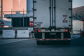 Semi truck parked at a loading dock with visible caution signs and industrial surroundings. HD wallpaper