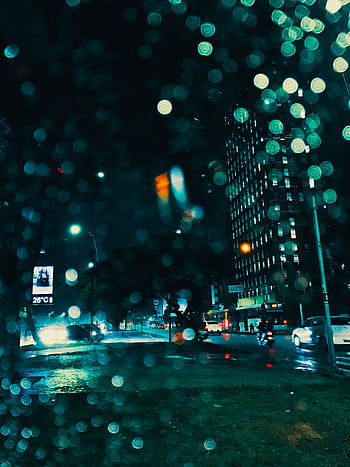 Dynamic urban night scene with illuminated skyscrapers and raindrops on window. HD phone wallpaper