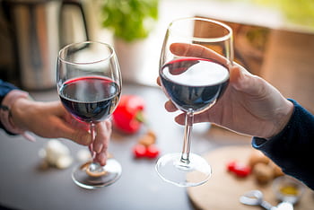 Two people toasting with red wine glasses on a dining table indoors. HD wallpaper