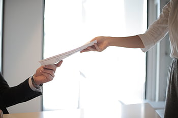Close-up of hands exchanging documents in a business setting indoors. HD wallpaper