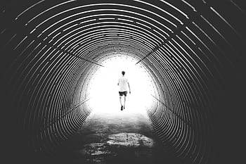 Silhouette of a man walking through a bright tunnel in Bellwald, Switzerland, captured in black and white. HD wallpaper