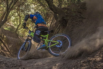 Mountain biker navigates a challenging off-road trail, kicking up dust in a forest setting. HD wallpaper