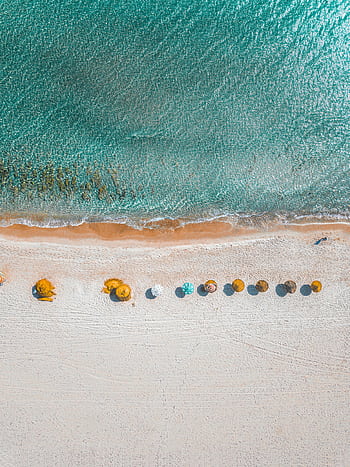 Aerial view of vibrant beach umbrellas on the shore with turquoise waves gently crashing. HD phone wallpaper