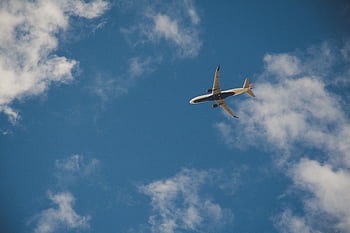 A commercial airplane flying high in the clear blue sky with clouds. HD wallpaper