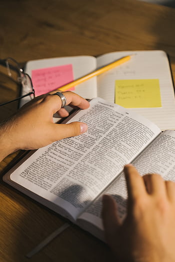 Close-up of hands holding and reading a Bible with study notes and a pencil on a desk. HD phone wallpaper