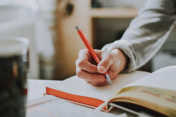 A person writing in a notebook with a red ballpoint pen, showcasing detail and focus. HD wallpaper