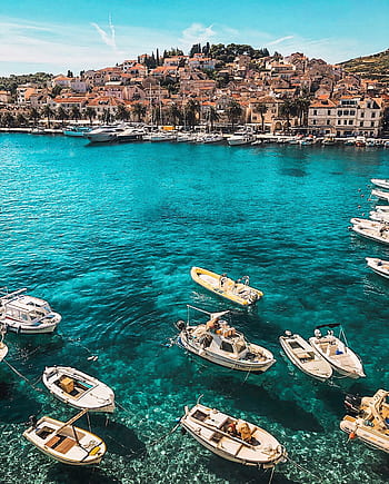 Boats in the vibrant blue waters of Hvar, Croatia, showcasing a charming coastal town under sunny skies. HD phone wallpaper