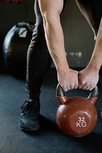 Athletic male lifting a kettlebell for strength training in an indoor gym. HD phone wallpaper