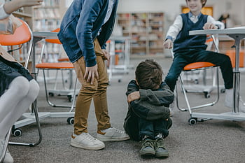 A young child sitting on the floor in a classroom facing bullying from peers. HD wallpaper