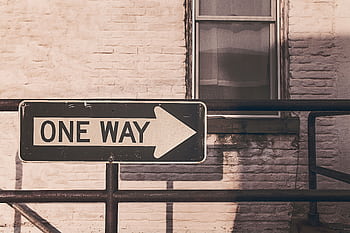 A vintage one way sign pointing right, mounted on a metal railing against a brick wall in urban setting. HD wallpaper
