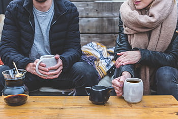 Two adults enjoying a cozy coffee break outdoors, wrapped in warm clothing. HD wallpaper
