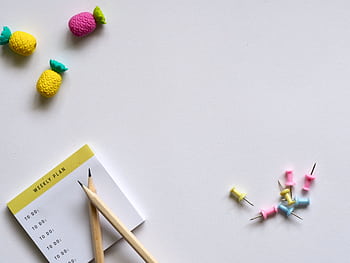 Flat lay of desk items including a planner, pencils, erasers, and push pins on a white background. HD wallpaper