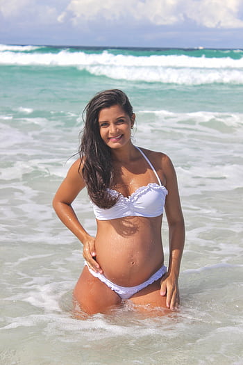 Pregnant woman in a white bikini enjoys sunny beach waves creating a serene and joyful moment. HD phone wallpaper