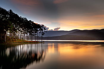 Stunning sunset over a calm lake with reflections of trees and distant hills. HD wallpaper
