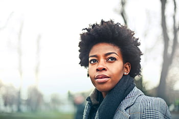 A fashionable black woman with an afro hairstyle in a winter coat poses outdoors in Budapest park. HD wallpaper
