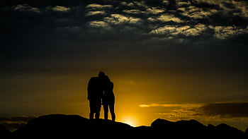 Silhouetted couple embracing at sunset, creating a romantic and serene atmosphere. HD wallpaper